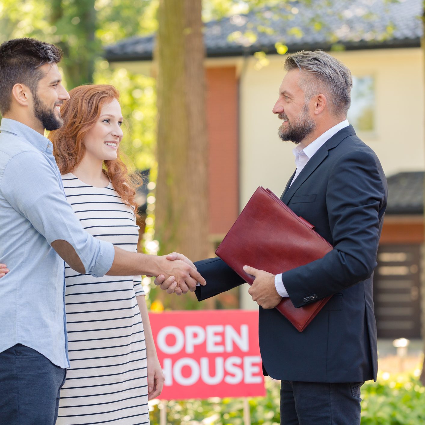 Real estate agent welcoming young smiling couple and inviting to presentation of house