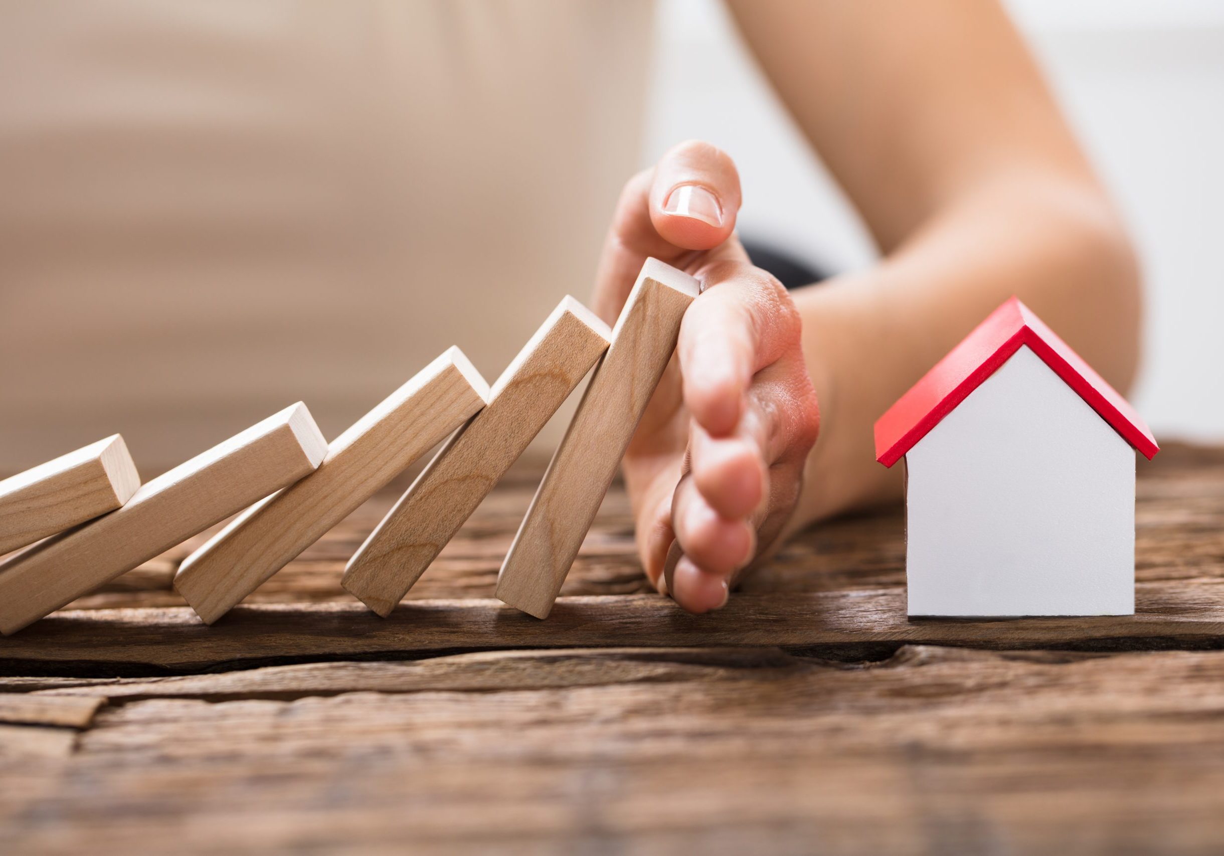 Close-up Of A Human Hand Stopping The Wooden Blocks From Falling On House Model